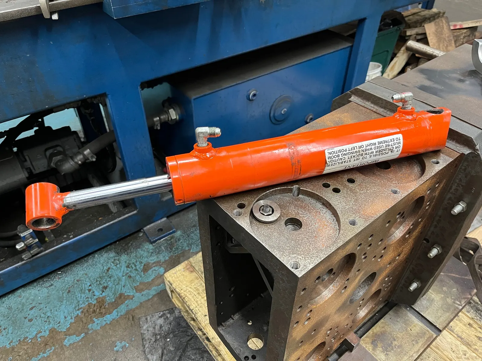 Bright orange hydraulic ram cylinder staged next to a freshly machined manifold block on the Reidville shop floor