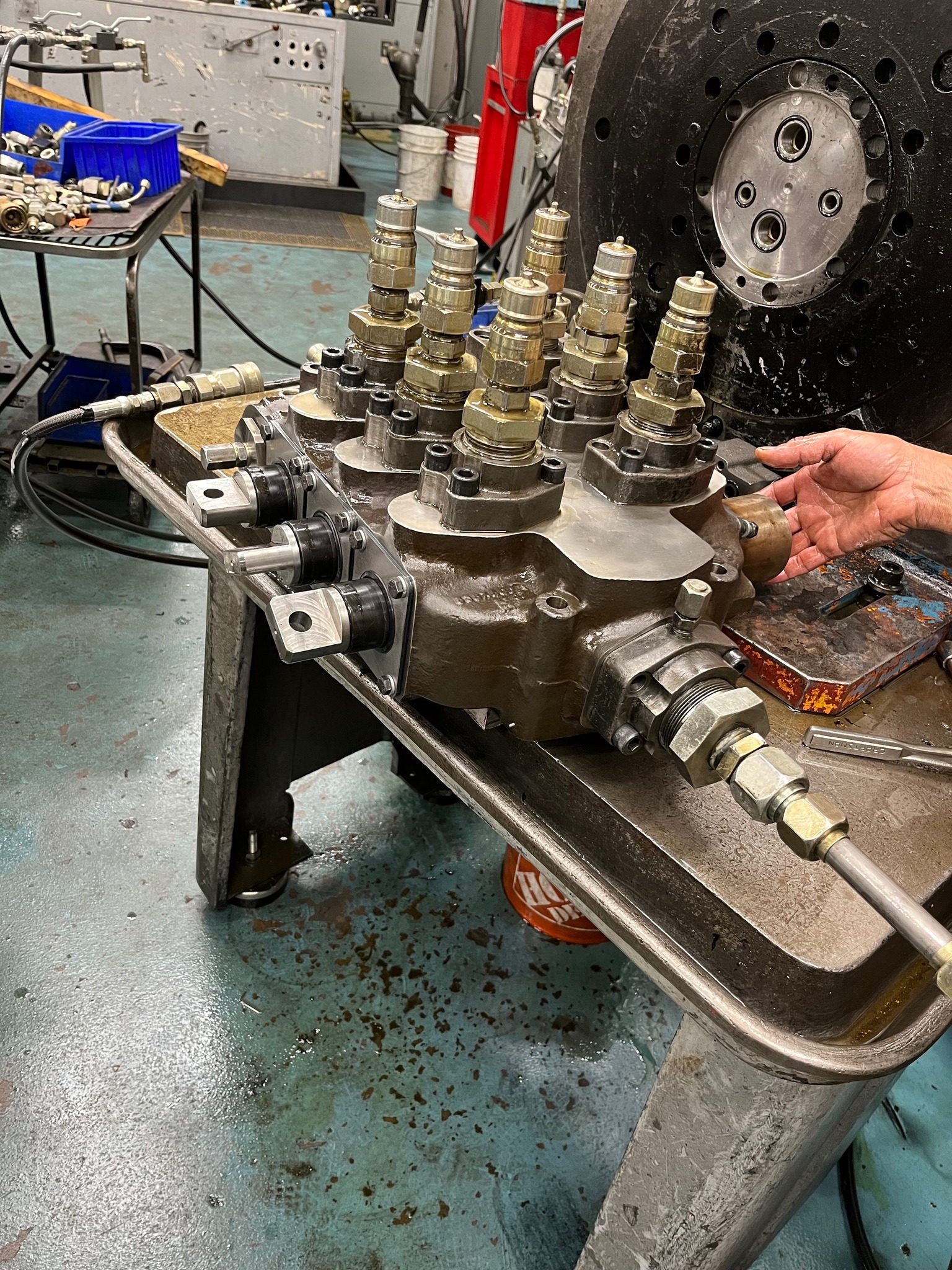 Hydraulic valve body on test stand with fittings installed, technician hand-checking assembly