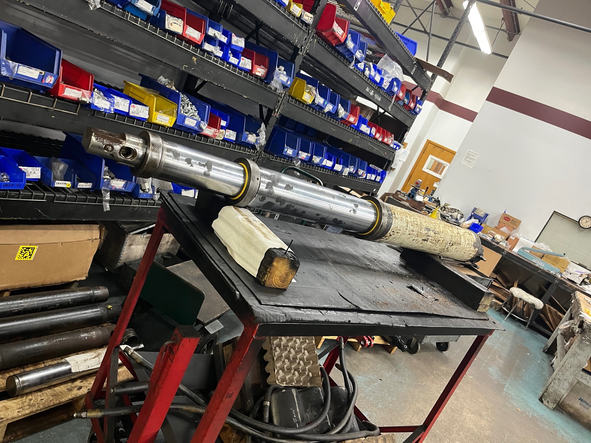 Reidville Hydraulics shop — chrome piston rod on workbench with parts shelves