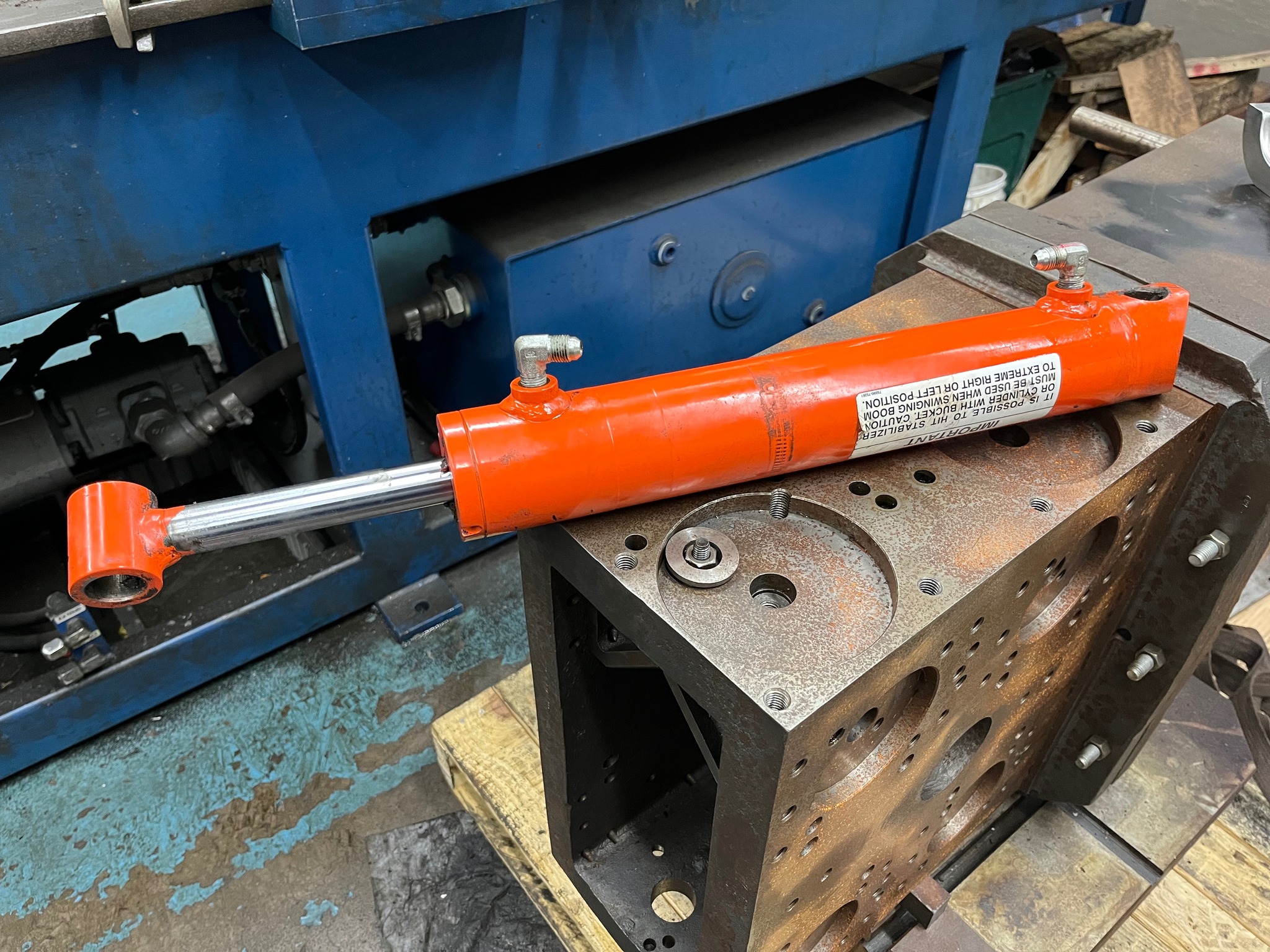 Bright orange hydraulic ram cylinder staged next to a freshly machined manifold block on the Reidville shop floor